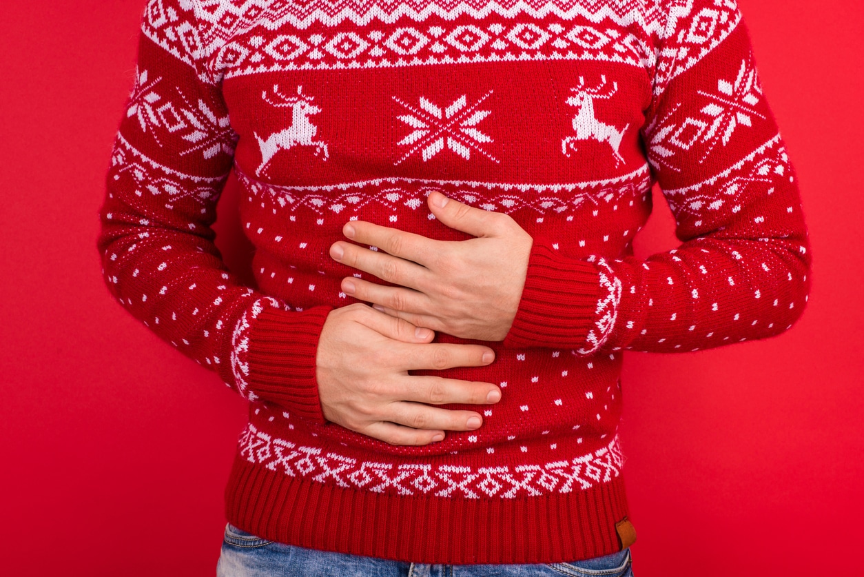 Close up photo of men in red winter sweater with deers holding his stomach isolated on red background